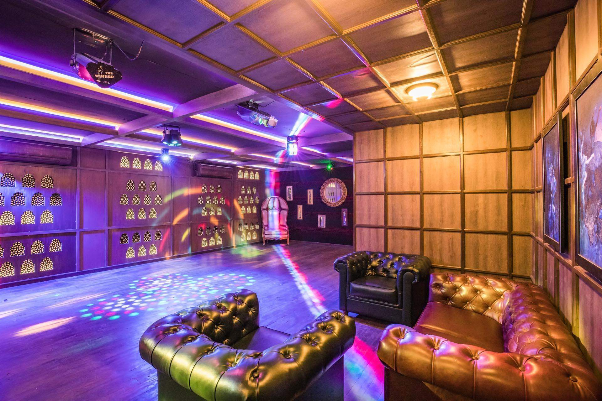 An indoor disco area at Ramsukh Resort with colorful lighting, wooden decor, leather sofas, and a dance floor for entertainment.